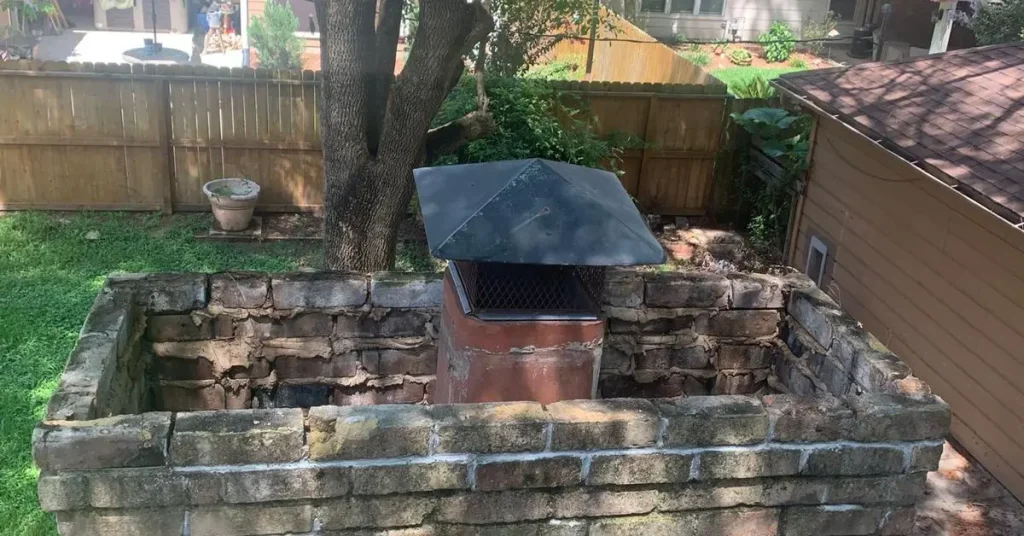 Damaged brick chimney stack with a metal cap and deteriorating masonry, showing issues that can affect chimney repair cost.